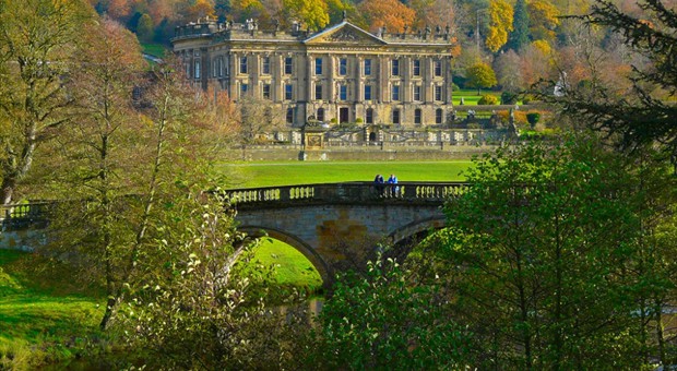 An English country house beyond an arched stone bridge, surrounded by trees in autumn colour